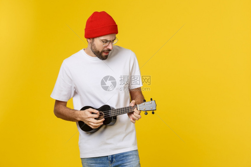 年轻英俊的吉他手工作室拍的黄色背景图片