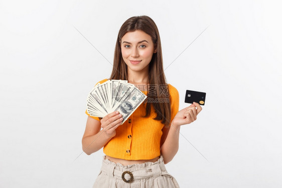 快乐的年轻女身处灰色背景一边看持有钱和信用卡一边看快乐的年轻女身处灰色背景图片