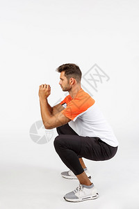 在运动服蹲下坐着和按紧握手以加强肌肉健身锻炼训练习垂直全长年轻男运动员在服蹲坐着和按紧以加强肌肉训练习图片