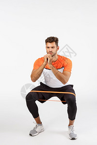 积极有重点的运动员用阻力绳子蹲下通过弯脚侧腰伸展设备坐下来拉伸设备坐双臂以保持良好的形状锻炼概念积极有重点的运动员用阻力绳子蹲下图片