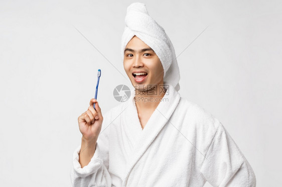 穿着浴袍和巾的英俊亚洲男子展示牙刷和笑早上洗脸准备大日子白背景美丽spa和休闲概念穿着浴袍和巾的英俊亚洲男子展示牙刷和笑图片