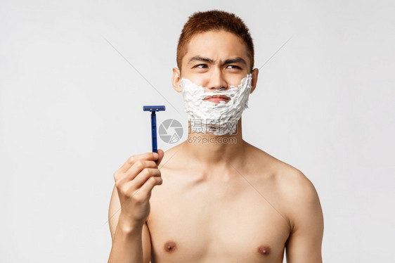 美丽人与卫生概念以赤裸的躯体向外看不想刮胡子但需要握着剃刀用不舒适的脸部涂面霜美人与卫生概念以裸的躯体用不舒适的脸部涂面霜图片