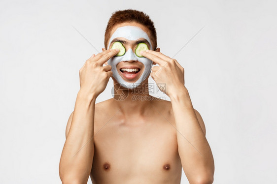 美护肤和spa概念热情放松的asin男子的肖像享受周末施用肛门治疗面部罩和涂上黄瓜眼睛笑得广泛白色背景美护肤和spa概念热情放松图片