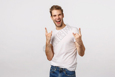 欢乐和的金发大胡子男穿着白色t恤衫展示重金属摇滚乐和微笑的姿态参加美妙的节日欢乐活动图片