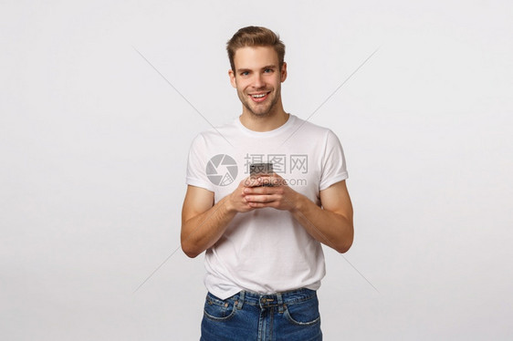电话数字现代生活技术概念英俊的金发男子穿白色t恤衫和牛仔裤手持智能机在小杂货店聊天看镜头电话技术概念英俊的金发卡男子看相机图片