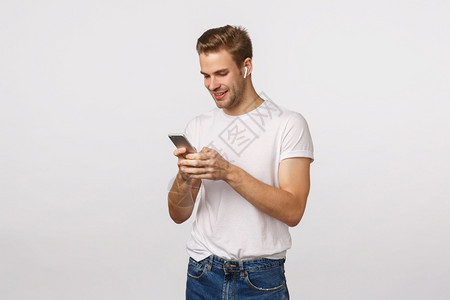 穿着白色t恤衫牛仔裤持有智能手机戴无线耳看移动显示阅读信息选歌白背景穿着色t恤背景背景图片