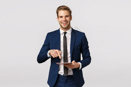 您必须看到这个喜悦优雅的男创业者在经典西装领带握着数字平板电脑指着工具屏幕来展示商业伙伴的绝佳新闻在线杂志您必须看到这一点喜悦的图片