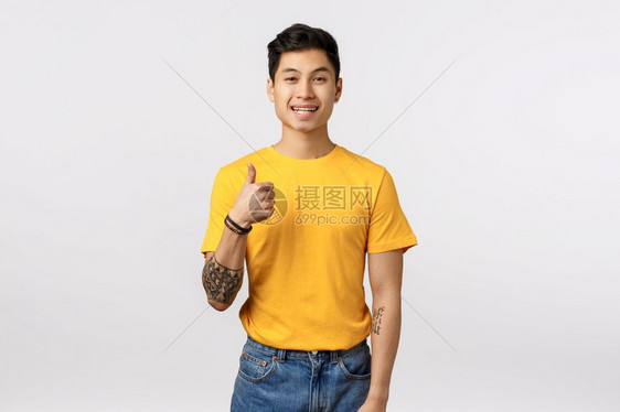 热情的英俊亚洲人纹身穿黄色t恤衫的纹身男子露出拇指像手势微笑点头同意你白背景好主意让我们来做吧热情的亚洲人纹身穿黄色t恤衫的纹身图片