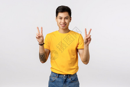 展示和平迹象胜利姿态欢笑的发出积极的气氛玩乐心情娱白人背景时尚的漂亮亚洲男人身上有黄色t恤的纹身微笑欢白人背景图片