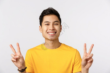 近身的年轻人穿着黄色t恤展示和平的标志欢笑容站在白色背景上表达幸福生活方式现代一和人的概念展现幸福的表情背景图片