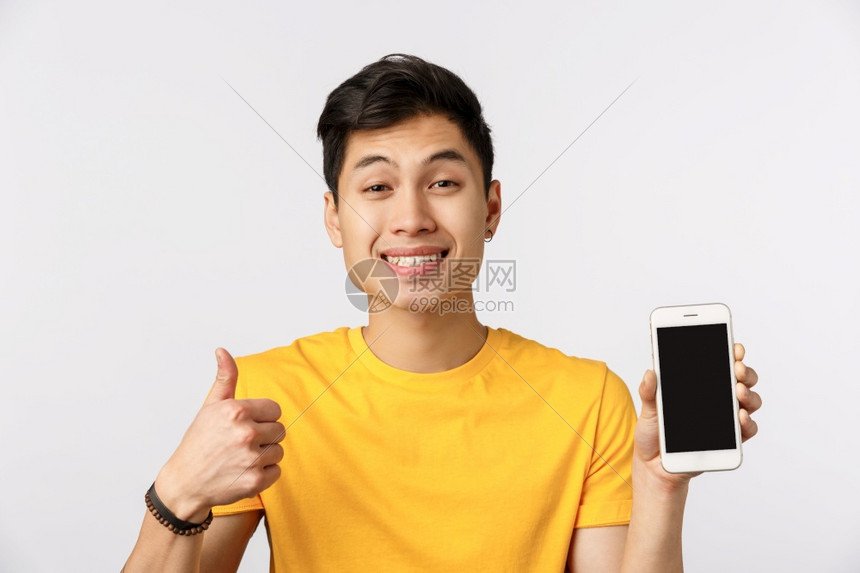 在黄色t恤衫上亲密的友好穿黄色t恤衫的亚洲男子在批准时展示拇指如手势显示智能机宣传在线网站公司横幅或社交页面简介白色背景近端的高图片