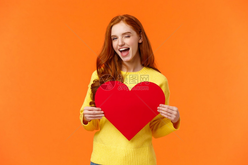情人节,男朋友和女的概念 可爱和的红发女人 拿着大牌和微笑,眨眼的红发女人,站立的橙色背景。图片