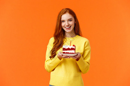 女孩在黄色毛衣上站立橙背景女朋友在黄色毛衣上狂欢派对带一块蛋糕和根蜡烛庆祝伴侣生日唱着快乐的b日笑着可爱站在黄色毛衣上的橙背景图片