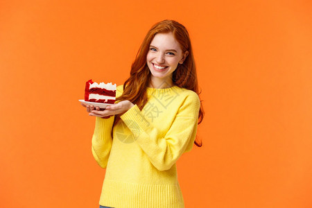 可爱的红发女人拿着美味自制的蛋糕笑着自制的一块蛋糕笑着分享咬对待朋友笑着庆祝生日或喜欢吃甜点橙色背景可爱的亲红发女人拿着美味自制图片