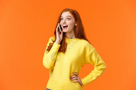 欢笑和惊讶的红头发女孩扩大眼睛并印象深刻听到朋友在电话交谈时的好消息把智能手机放在近耳边交谈橙色背景欢笑和惊讶的红头发女孩扩大眼图片