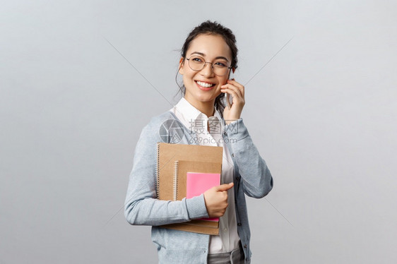 带着眼镜的女孩手上抱着笔记本一边打电话图片