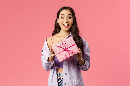 兴奋的年轻亚洲女孩带着礼物拿包裹盒祝贺假日或生被邀请参加今天的晚会站着愉快的粉红色背景为你准备了礼物兴奋的年轻亚洲女孩拿着包裹盒图片