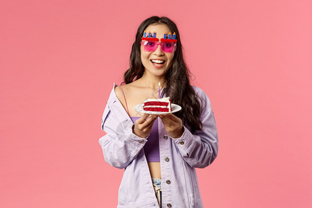 欢庆节假日和人的概念欢庆快乐的亚洲生日女孩微笑穿着有趣的白日眼镜和吃蛋糕在吹蜡烛上许愿看着兴奋的相机粉红背景图片