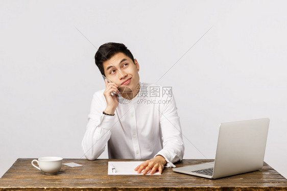 穿着白衬衫坐在办公室的桌子上手持笔记本电脑报告文件和咖啡杯笑不满意谈论一些不愉快的电话穿着白衬衫嘲笑不满意谈论一些不愉快的电话图片