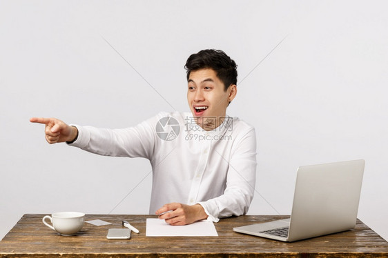 穿着白衬衫坐在笔记本电脑文件向左指嘲笑有趣的同事嘲笑白人背景哈看着穿白衬衫指左人背景的喜乐和娱人办公室经理图片
