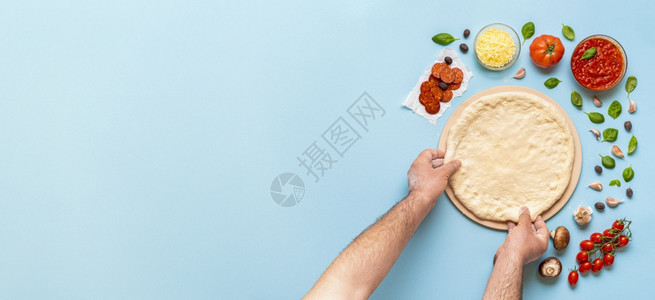 man手准备比萨面团在视图上方无法辨认的人正在蓝厨房桌上做比萨一步地做比萨图片