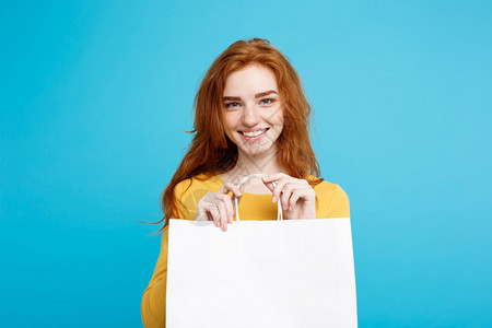 年轻漂亮的红头发女孩带着白色购物袋微笑蓝面纸背景图片