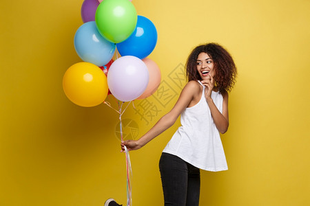 庆祝概念关闭快乐的年轻非洲美女肖像穿着白色t恤彩的派对气球黄色的面粉工作室背景关闭快乐的年轻美丽非洲女肖像穿着彩色的派对气球黄色图片