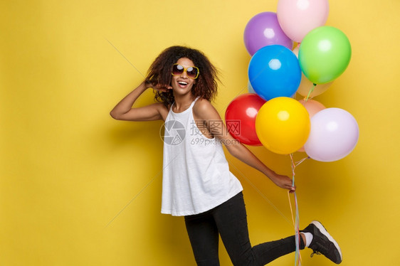 庆祝概念关闭快乐的年轻非洲美女肖像穿着白色t恤彩的派对气球黄色的面粉工作室背景关闭快乐的年轻美丽非洲女肖像穿着彩色的派对气球黄色图片