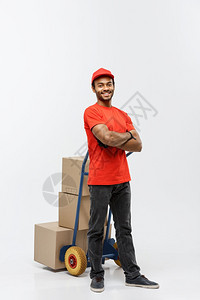 交付概念英俊的非洲送货员或运用一堆箱子推运手车的肖像在灰色工作室背景上隔离复制空间交付概念英俊的非洲送货员或运用一堆箱子推运手车图片