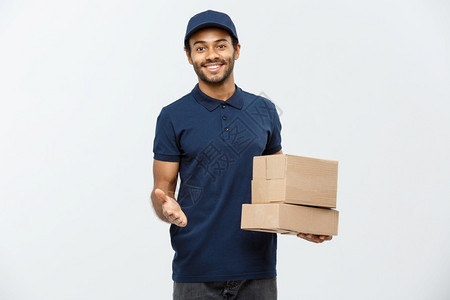 交付概念快乐的非洲送货员肖像指向展示盒包的手势孤立在灰色工作室背景上复制空间快乐的非洲送货员肖像指向展示盒包图片
