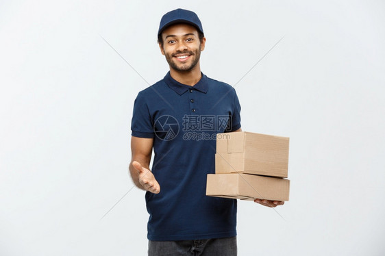 交付概念快乐的非洲送货员肖像指向展示盒包的手势孤立在灰色工作室背景上复制空间快乐的非洲送货员肖像指向展示盒包图片