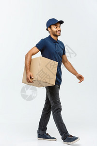 交付概念快乐的非洲送货员蓝布行走向客户发送盒套件的肖像以灰色工作室背景隔离复制空间图片