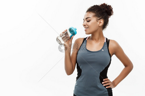 健康和身概念健身后穿着运动服装喝饮用水的美丽女孩在白色工作室背景上隔离健身后穿着运动服装喝饮用水的美丽女孩图片