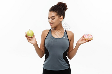 健康饮食概念美丽的运动非洲国人在甜圈和绿苹果之间做决定孤立在白色背景上健康和饮食概念美丽的运动非洲国人在甜圈和绿色苹果之间做决定图片