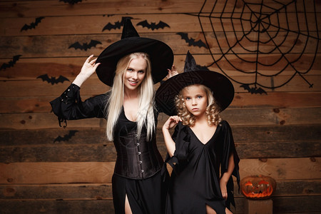 万圣节装扮halowen概念快乐的母亲和女儿穿着巫服庆祝halowen装扮有弯曲南瓜的圣殿在木制工作室背景上的蝙蝠和蜘蛛网之上打扮成弯曲南背景