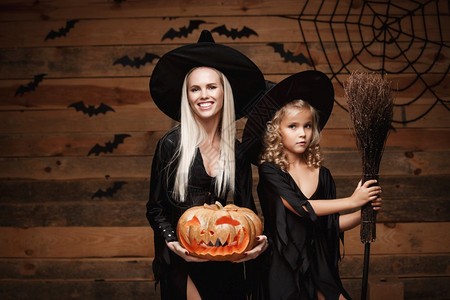 halowen概念快乐的母亲和女儿穿着巫服庆祝halowen装扮有弯曲南瓜的圣殿在木制工作室背景上的蝙蝠和蜘蛛网之上打扮成弯曲南图片
