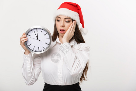 时间管理概念戴着圣塔帽的年轻商业妇女时钟与白种背景隔绝图片