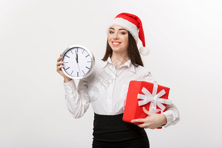 时间管理概念带圣塔帽的年轻商业妇女时钟与白色背景隔绝图片