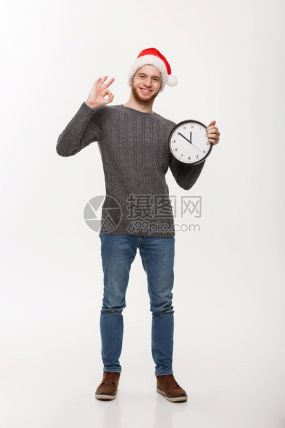 假期概念年轻英俊的胡子男穿着毛衣白色时钟给好牌图片
