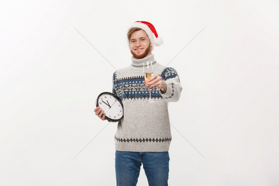 假期概念年轻英俊的胡子男穿着毛衣白色时钟和香槟白色工作室背景图片