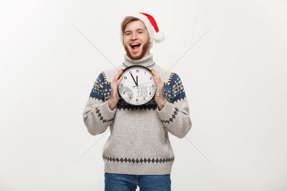 假期概念年轻快乐的英俊长胡子男穿着毛衣白色时钟工作室背景图片