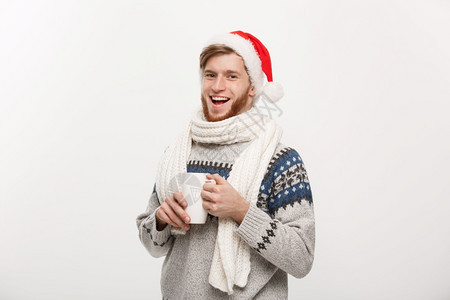 圣诞概念穿着毛衣和圣塔帽的年轻胡子男拿着热咖啡杯图片