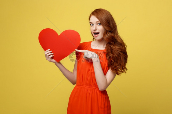 情人节和生活方式概念一位身着红衣的有吸引力年轻女肖像她用手指着纸心与黄色工作室背景隔绝情人节和生活方式概念一位身着红衣的有吸引力图片