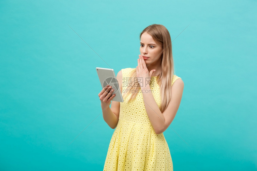 一位令人惊讶的年轻女士在看一个蓝色工作室背景的数码平板电脑图片