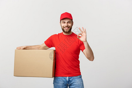 快乐的年轻送货员站在红帽子上与包裹邮箱隔绝在白色背景上表现良好快乐的年轻送货员站在红帽子上包裹邮箱在白色背景上表现良好图片