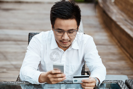 英俊的青年男子享受用信卡在移动电话上购物的乐趣图片