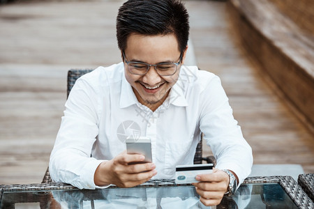 英俊的青年男子享受用信卡在移动电话上购物的乐趣图片