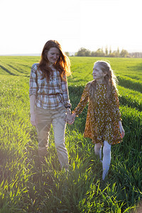 日落时家庭幸福的母亲和女儿在田野上行走图片