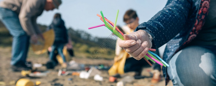 露出在沙滩上收集的少数稻草和一些在背景中工作的志愿者有选择地聚焦在前景中的稻草图片