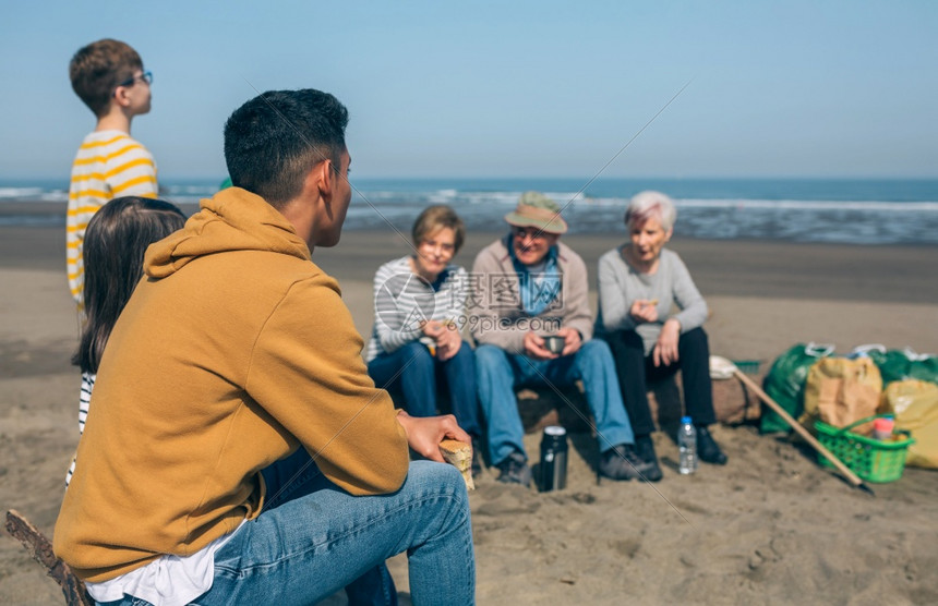 在清理海滩后休息和吃东西观众们集中关注在前景下的人在清理海滩后休息的志愿者图片